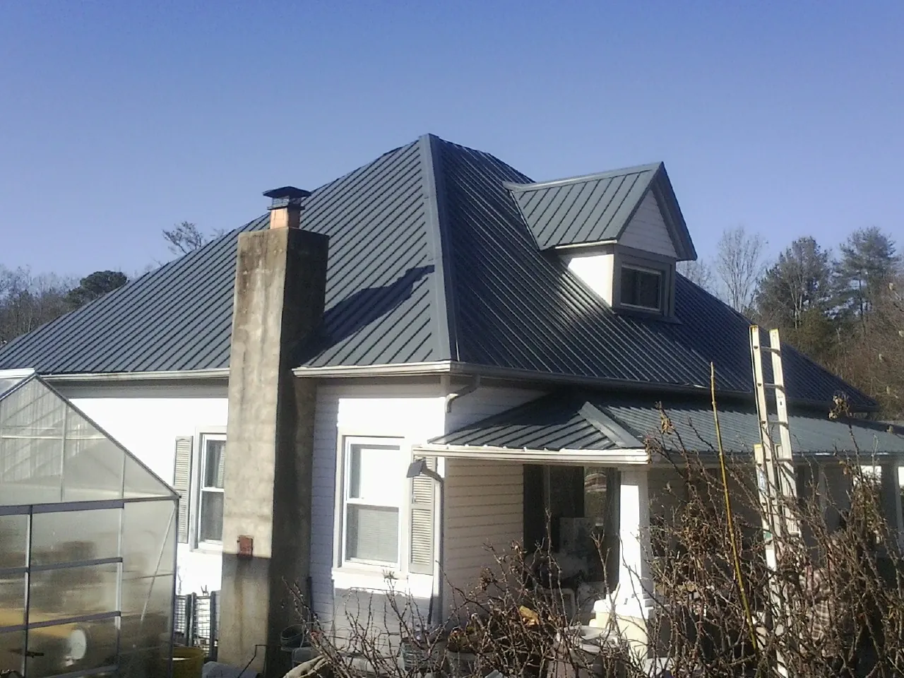 Dark blue standing seam metal roof on a white farmhouse with dormer — Slate & Tile Roof Repair by Roofing Brothers in Napoleonville
