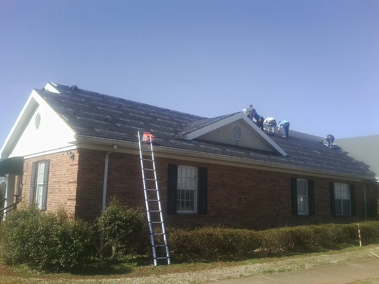 Crew tearing shingles off a brick ranch roof with a ladder set — Emergency Roof Repair work by our crew in Napoleonville