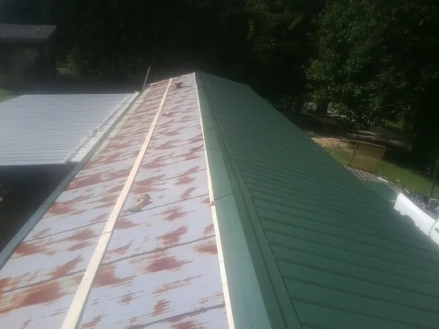 Old rusted panels beside newly installed green metal roofing — Wind Damage Roof Repair by Roofing Brothers in Napoleonville