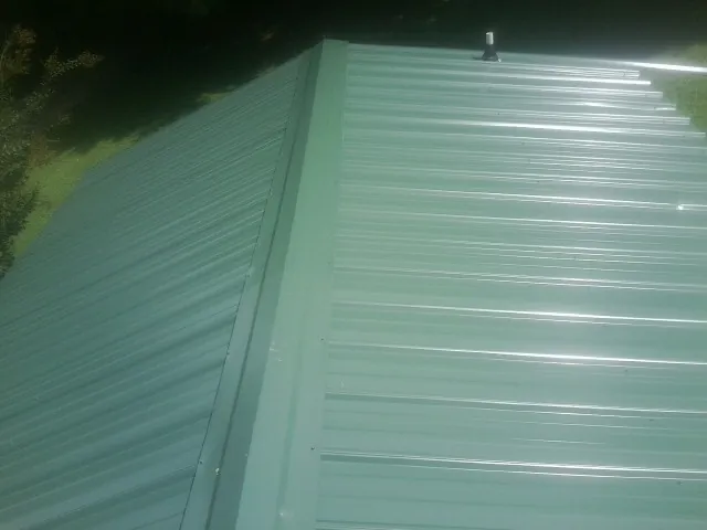 New green metal panels meeting at the ridge of a roof — Flat Roof Repair work by our crew in Napoleonville