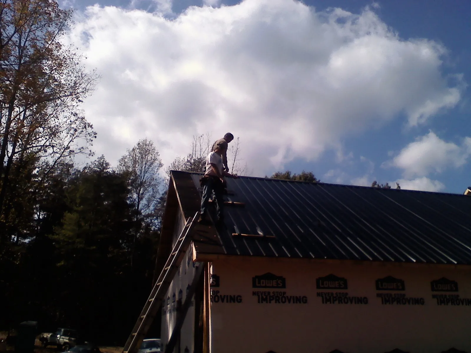 Roofer fastening dark metal panels high against a cloudy sky, from a Roof Inspection job in Napoleonville