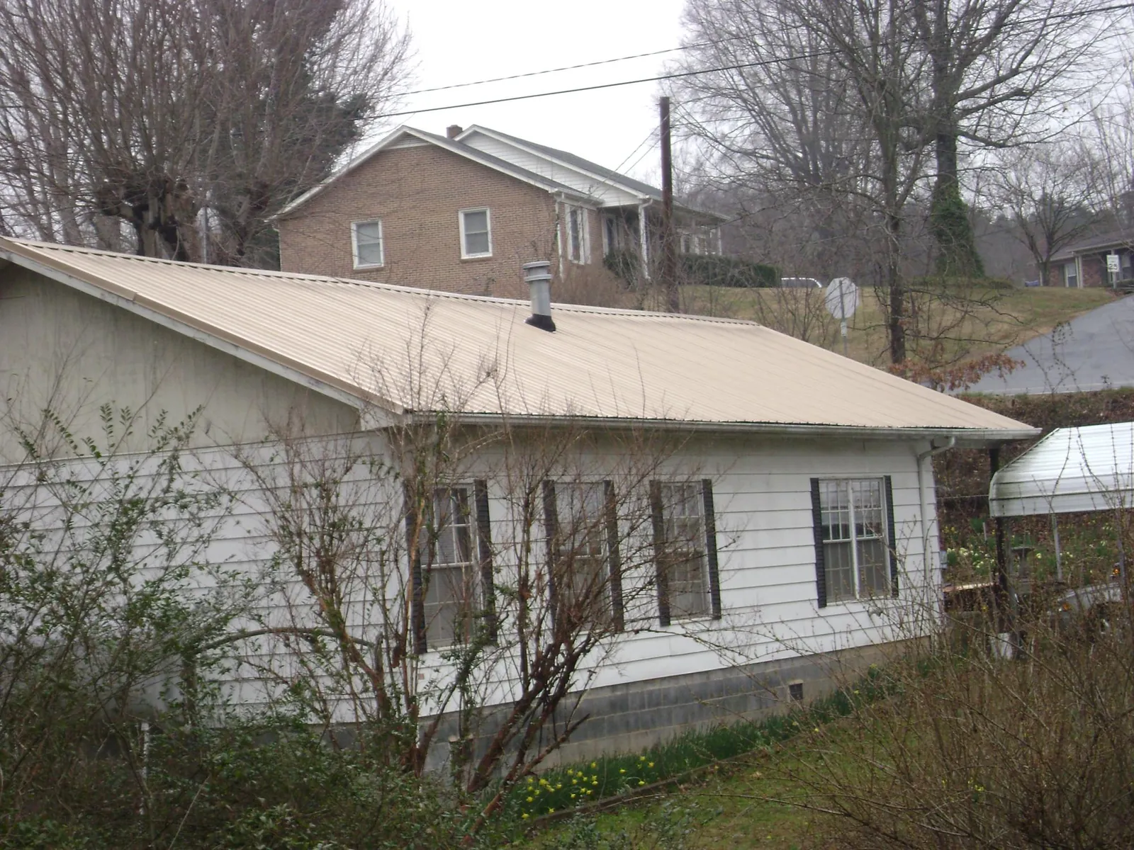 Tan metal roof on a white sided house set into a hillside — Commercial Roofing by Roofing Brothers in Napoleonville